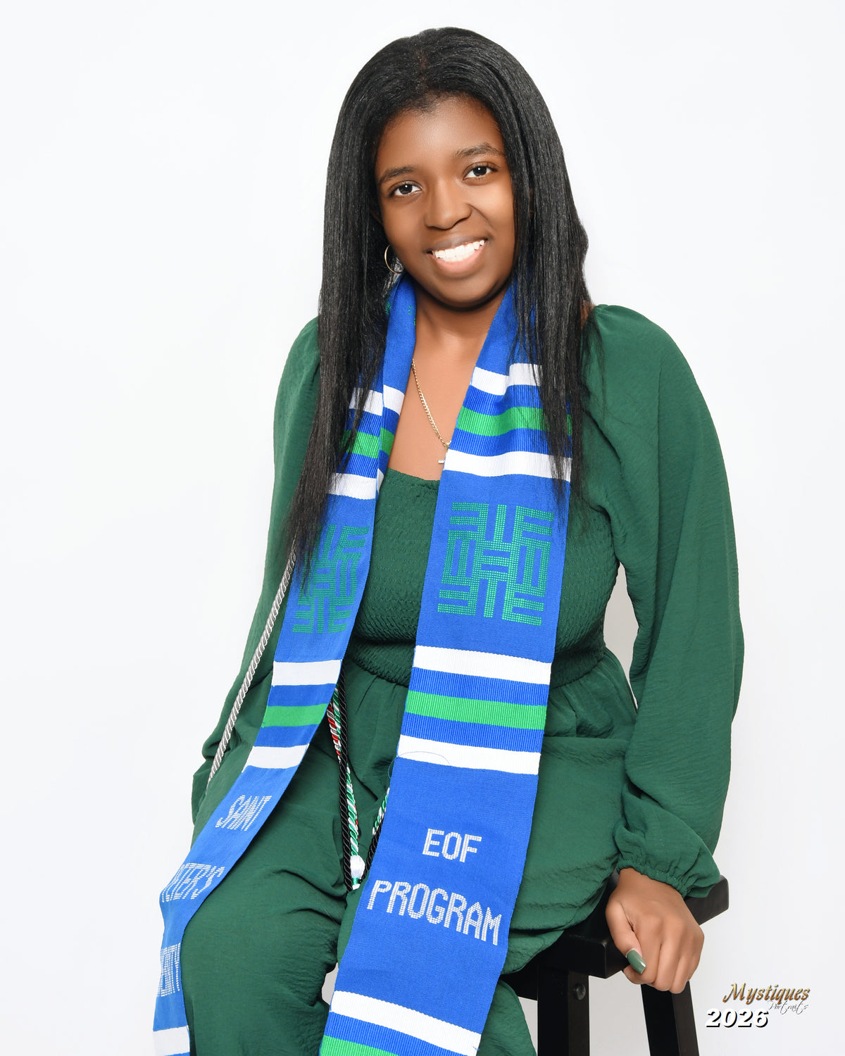 Woman wearing a green outfit with a blue and green scarf, sitting on a white background.